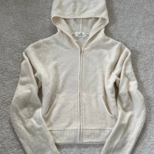 Beige hoodie i stickat från H&M - Mysig beige hoodie från H&M i stickat material. Tröjan har dragkedja framtill, huva och två fickor. Perfekt för lager-på-lager och chill dagar. Långärmad och med ribbade muddar för extra komfort.