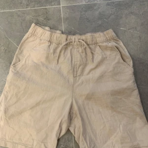 Beiga shorts med snörning från Kappahl - Snygga beiga shorts från Kappahl med elastisk midja och snörning framtill. Modellen har två sidofickor och två bakfickor, perfekt för chill dagar. Lätta och sköna i bomull, passar grymt till sommaren.