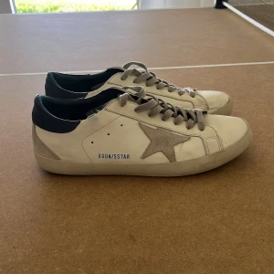 Golden Goose sneakers - Snygga vita sneakers från Golden Goose, grå snörning och en beige stjärna på sidan. Skicket är bra, lite slitna i sulans kanter (bild 3-4) därav priset. Allmänt bra skick