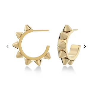 Guldiga örhängen med nitar - Coola guldiga hoops med spetsiga nitar runt hela örhänget. De har en chunky känsla och ger en edgy vibe till din look. Perfekta för dig som vill sticka ut och addera lite attityd till outfiten.
