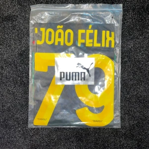 AC Milan x Off-White João Félix Puma S - AC Milan x Off-White fotbollströja från Puma i svart och grön med gula detaljer och tryck. Nummer 79 och João Félix på ryggen. Snygga röda detaljer på ärmslut och krage, samt Off-White-mönster över hela tröjan. Materialet är lätt och andas, perfekt för match eller träning.