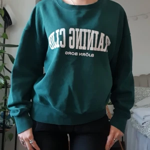 Grön sweatshirt från Björn Borg - Mörkgrön sweatshirt från Björn Borg med vit text 'TRAINING CLUB' framtill. Tröjan har en klassisk rund halsringning och långa ärmar. Mjuk insida och relaxed fit, perfekt för chill dagar eller träning. Snygg och enkel att matcha med jeans eller tights. Strlk M men passar som en S/XS 