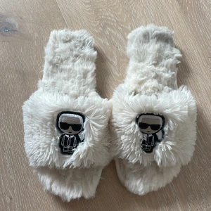 Fluffiga vita tofflor karl Lagerfeld  - Supermjuka och fluffiga tofflor i vit färg med en broderad patch framtill, karl lagerfelds logotyp .todflorna säkjes i befintligt skick