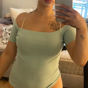 Ljusgrön offshoulder topp - Snygg ljusgrön topp med offshoulder-design och korta ärmar. Enkel och stilren modell som sitter tight och framhäver axlarna. Perfekt för dig som gillar en clean look med lite edge.