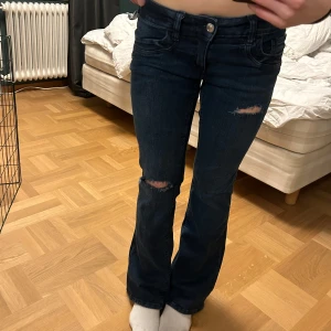 Mörkblå jeans med slitningar - Säljer ett par mörkblå jeans med slitningar på knäna. De har en bootcut-stil och är lågmidjade. Perfekta för en avslappnad look. Aldrig använda bara testade. Skriv om ni har fler frågor🫰