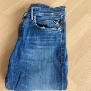 Blå Replay Anbass jeans slim fit - Snygga blå Replay Anbass jeans med klassisk femficksdesign och diskreta slitningar. Jeansen har slim fit-passform, normal midja och är tillverkade i mjukt stretchigt denim för extra komfort. Perfekta för dig som gillar en modern och stilren look. Dom är i fint skick och använda men inga skador eller liknande