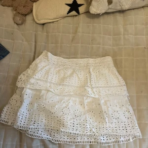 Vit volangkjol med broderade detaljer - Säljer en söt vit kjol med volanger och broderade blommönster. Kjolen har en luftig känsla och är perfekt för varma dagar. Resår i midjan för extra komfort och fin passform. Storleken är 13-14 men passar som en s 
