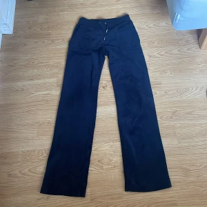 Svarta mjukisbyxor från Juicy Couture - Säljer ett par svarta mjukisbyxor från Juicy Couture med broderad logga på ena fickan. Byxorna har normal passform och raka, vida ben. Perfekta för en avslappnad och trendig look. 