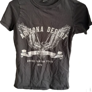 Svart t-shirt med Arizona-tryck från Gina Tricot - Snygg svart t-shirt från Gina Tricot med ett coolt Arizona Desert-tryck i grått. T-shirten har korta ärmar och rund halsringning, perfekt för en avslappnad stil. Materialet är mjukt och bekvämt, vilket gör den idealisk för vardagsbruk.💕💕