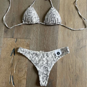 Beige bikini med ormmönster - Trendig bikini från bikbok i beige med ormmönster. Triangeltopp med knyt i nacke och rygg samt matchande bikinitrosa. Perfekt för stranden eller poolen.