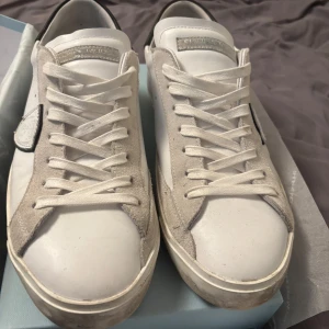 Vita sneakers från Philippe Model med svarta detaljer - Säljer ett par vita Philippe Model prsx low sneakers med svarta detaljer på hälen och grå mockadetaljer längs sidorna. Perfekta för en stilren look. Köpta från merchsweden storlek 44 och har knappt används pga för stora. Bara att fråga om mer bilder och information