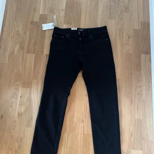 Svarta jeansbyxor från Nudie Jeans - Säljer ett par svarta jeansbyxor från Nudie Jeans, modell Slim Adam. Klassisk femficksdesign med knapp- och dragkedjegylf. Snygg, enkel stil som passar till det mesta. Märkeslapp och tags sitter kvar.