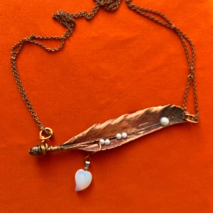 Halsband med kopparfärgat blad och pärlor - Unikt halsband med ett kopparfärgat elektropläterat fågelfjäderbladshäng, dekorerat med små vita pärlor och ett vitt hjärtformat hänge. Kedjan är gjord av metall och har en varm vintagelook.