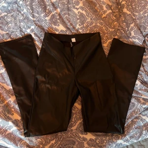 Svarta skinnbyxor med slits - Snygga svarta byxor i skinnimitation med tight passform, lite utsvängda med slits nertill på benen. Perfekta för att lyfta vilken outfit som helst.