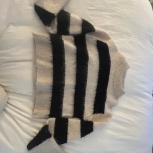 Randig mohairtröja från H&M - Säljer en fluffig och mysig stickad tröja från H&M i mohair- och ullblandning. Tröjan är beige med breda svarta ränder, har lång ärm och ribbade muddar. Perfekt för kyliga dagar och superenkel att styla till jeans eller kjol.