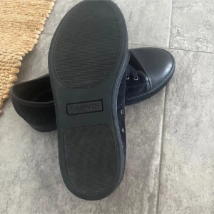 Svarta Lanvins - Säljer ett par svarta sneakers från Lanvin med ovandel i mocka och detaljer i skinn. Skorna har snörning, rund tå och platt sula. Perfekta för dig som gillar stilrena och lyxiga sneakers. 