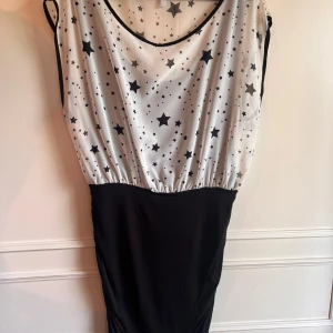 Svart och vit klänning med stjärnmönster från Only - Snygg klänning från Only med ett stjärnmönstrat överdel i vitt och svart. Klänningen har en v-ringad design och är ärmlös, vilket ger en stilren look. Perfekt för en kväll ute eller en speciell tillställning.