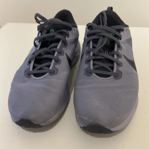 Lila Nike sneakers - Säljer ett par grå Nike sneakers med snörning och svarta detaljer. Skorna har en bekväm sula med gröna inslag och är perfekta för träning eller vardagsbruk.
