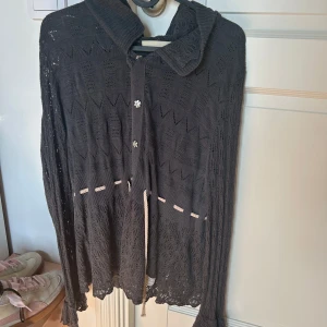 Svart/grå  spetskofta från Odd Molly - Säljer en elegant svart spetskofta från Odd Molly med fina knappar och knytband framtill. Koftan har ett vackert mönster och långa ärmar, perfekt för att lägga till en touch av stil till din outfit. Storlek 4