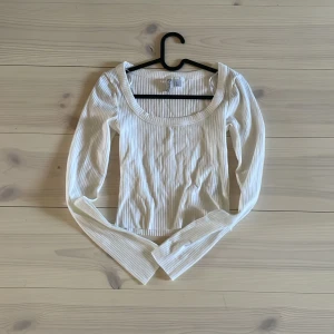 Vit ribbad topp från H&M - Säljer en stilren vit ribbad topp från H&M med långa ärmar och rund halsringning. Perfekt för lager-på-lager eller som den är. Passar till många olika stilar och tillfällen.