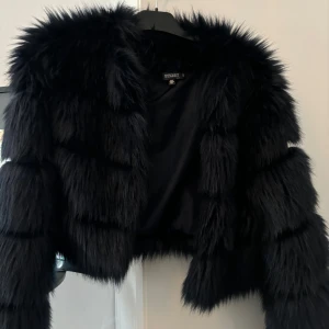Svart pälsjacka från Missguided - Snygg svart pälsjacka från Missguided med en lyxig look. Jackan har en croppad design och långa ärmar, perfekt för att hålla sig varm och stilren under kyliga dagar. Den är tillverkad i syntetmaterial och har en mjuk och fluffig textur.