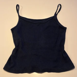 mörkblå ribbad linnetopp från brandy melville - Säljer en mörkblå ribbad linnetopp med smala axelband. Toppen har en enkel och stilren design, perfekt att matcha med olika outfits. Materialet är mjukt och stretchigt för en bekväm passform.