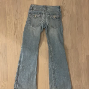 Ljusblå bootcut jeans från Gina Tricot - Säljer ett par ljusblå jeans från Gina Tricot med bootcut-modell. Byxorna har klassiska fickor bak med lock och knapp, samt dragkedja och knapp framtill. Perfekta för dig som gillar en lite utsvängd stil. För barn och köpt på Gina Young i storlek 134