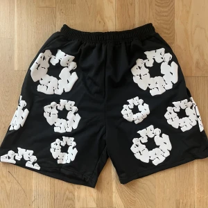 Svarta shorts med vita blommönster - Svarta shorts med elastisk midja och stora vita blommönster över hela tyget. Perfekta för en avslappnad stil och sticker ut med sitt unika tryck.