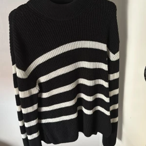 Svart och vit randig stickad tröja - Säljer en svart stickad tröja med vita horisontella ränder och medelhög krage. Tröjan har lång ärm och är gjord i ett grovstickat material som känns både trendigt och bekvämt. Perfekt för lager-på-lager-stil. Är i stl XS sitter som en S