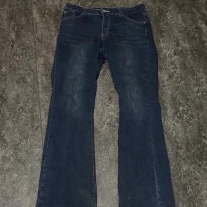 Blå bootcut jeans med broderade fickor - Snygga blå bootcut low/mid waisted jeans med broderade detaljer på bakfickorna. Perfekta för en avslappnad stil med en touch av unik design. Klassisk femficksmodell med knapp och dragkedja framtill. Jeansen är även stretchiga så går att passa från L-XXL. Tyvärr har jeansen ett litet hål vid högra delen nere men den syns inte alls! Den går även att fixa genom att sy ifall man känner att det behövs. Pris och mer info kan diskuteras !! 