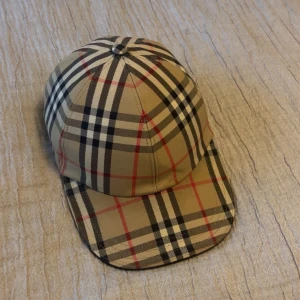 Rutig keps från Burberry - Hej säljer nu min burberry keps som jag köpte på farfetch för ett nypris på 3600kr, nu efter ett halv år känner jag att jag ej har någon användning av den, den är i nästn helt nytt skick och passar de allra flest kepsen har en justerbar rem baktill för perfekt passform. Perfekt accessoar för en stilren look. Tveka ej på att höra av er vid frågor!