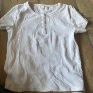 Vit ribbad topp med knappar från 152/11Y - Säljer en vit ribbad topp med korta ärmar . Toppen har knappar framtill som en fin detalj. Perfekt till sommaren och enkel att matcha med olika outfits. Passar som xxs också 