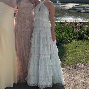 Vit långklänning med spets och halterneck - Säljer en romantisk vit långklänning med halterneck och vackra spetsdetaljer. Klänningen har volanger i flera lager och en feminin siluett, perfekt för sommarens speciella tillfällen. Använd en gång men kemad!