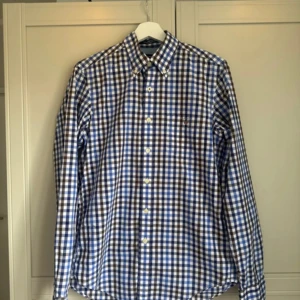 Blårutig skjorta från GANT - Säljer en snygg blårutig skjorta från GANT i bomull. Skjortan har en klassisk krage och knappar framtill. Perfekt för en stilren look. 💙 storlek S