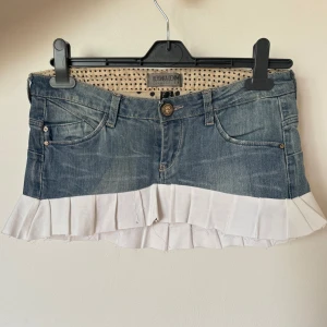 Lågmidjad jeanskjol med volang från Bershka - Superfin kort jeanskjol från Bershka med ljusblå denim och vit volang nedtill. Kjolen har klassiska jeansdetaljer som fickor fram och bak samt knapp och dragkedja. Liten i storlek, passar mig som har xs/s. Omsydda jeans noggrant! 