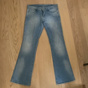 Ljusblå bootcut jeans från Wrangler - Säljer ett par low waist ljusblå bootcut jeans från Wrangler. Storlek 27/30. Mått: Midja: 38 cm, livhöjd: 20 cm, innerbenslängd: 73 cm, total längd: 91 cm