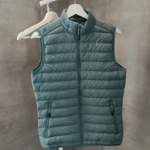 Dunväst från Strova - Snygg grön dunväst från Strova med ståkrage. Lättviktsquiltad design. Två fickor. Lätt figurformad. Kameran gör inte färgen rättvis = snyggare i verkligheten. Sista bilden mest sann = turkos mot grön