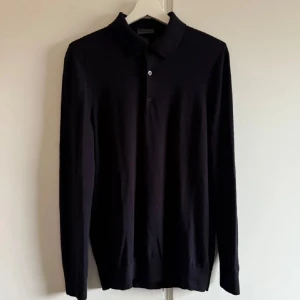 Långärmad piké - Säljer en stilren marinblå tröja från H&M i slim fit. Tröjan är tillverkad av 100% ull och har långa ärmar samt en klassisk krage med knappar. Perfekt för en elegant och bekväm look. Helt slutsålda på hm hemsida