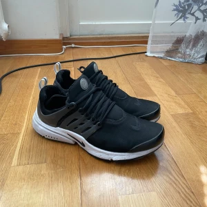 Svarta Nike sneakers - Säljer ett par svarta Nike sneakers med vit sula och snörning. Skorna har en modern design med en rund tå och är perfekta för både träning och vardag. De har en bekväm passform och är lätta att ta på och av med hjälp av hällor baktill.