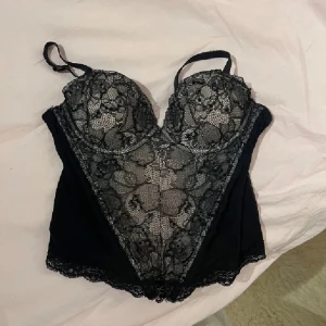 Svart spetskorsett - Elegant svart korsett med vacker spetsdetalj och justerbara axelband. Meshen har litet hål på men bara det yttersta lagret. Syns inte när man har på den