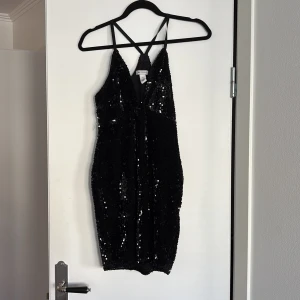 Svart paljettklänning från NLY One - Snygg svart klänning från NLY One med glittrande paljetter och smala axelband. Perfekt för en kväll ute! Klänningen har en v-ringad design och är kort i modellen.