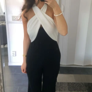 Svart och vit oneshoulder jumpsuit - Snygg svart och vit oneshoulder jumpsuit med en unik omlott-design. Perfekt för en kväll ute eller en speciell tillställning. Den har en elegant passform som framhäver figuren. Endast använd en gång, står ej varumärket 