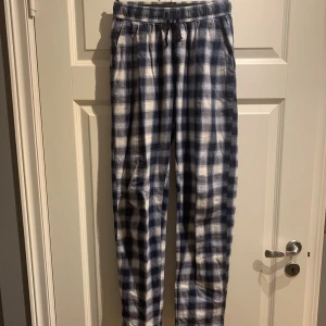 Rutiga mjukisbyxor blå/vit 158/164 - Mysiga mjukisbyxor i blått och vitt rutmönster med resår och snörning i midjan. Byxorna har raka ben och är tillverkade i mjukt bomullstyg, perfekta för chill dagar hemma. Fickor på sidorna för extra bekvämlighet.