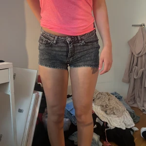 Svarta jeansshorts med tvättad look - Snygga svarta jeansshorts med tvättad, lite gråaktig finish. Modellen är lågmidjad och har klassiska fem fickor, bälteshällor och knappstängning. Perfekta till sommaren och passar till allt. Kort och tight passform för en trendig vibe.