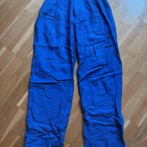 Blå linnebyxor från Lindex, strl 34 - Snygga blå linnebyxor från Lindex i storlek 34. Byxorna har avslappnad passform, resår i midjan och raka ben. Perfekta för varma dagar när du vill ha något luftigt och bekvämt. Färgen är riktigt klarblå och materialet är mjukt linne. 