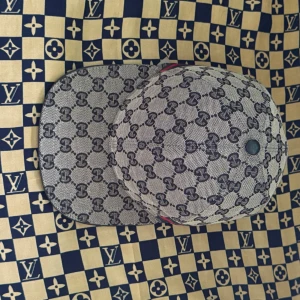 Gucci keps med GG-mönster - Snygg keps från Gucci i beige och svart med klassiskt GG-monogram över hela kepsen. Justerbar rem baktill i skinn och röd-grön detalj. Tillverkad i bomull och polyester, perfekt för dig som vill sticka ut med en lyxig accessoar.