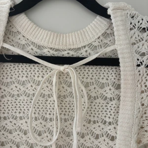 Vit stickad kofta med knyt från Chiquelle - Supersöt vit/cremevit stickad bikini cover-up från Chiquelle i storlek XS/S. Koftan har ett öppet virkat mönster, lång ärm och snygg knytning i ryggen. 