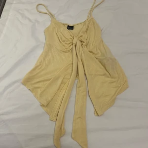 Beige linnetopp från Gina Tricot - Supersöt gul  linnetopp från Gina Tricot med smala axelband och snygg knytning framtill. Toppen har en flowy passform med asymmetrisk nederkant och är perfekt för varma dagar. Mjuk och lätt i materialet, riktigt skön att bära.