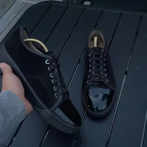 Svarta sneakers från Lanvin i mocka och lack - Snygga svarta sneakers från Lanvin med ovandel i mocka och glansiga lackdetaljer på tån. Klassisk låg modell med svarta snören och rund tå. Perfekta för dig som gillar stilrena men ändå unika skor.