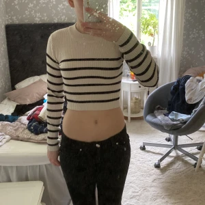 Randig croppad tröja från 157 - Säljer en croppad, ribbstickad tröja från 157 i beige med svarta ränder. Tröjan har lång ärm, rund halsringning och sitter tight. Perfekt för dig som gillar en trendig och stilren look. Är inte riktigt min stil längre, sitter väldigt skönt på huden eftersom tyget är mjukt! Är inte använd jättemånga gånger. 